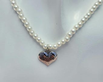 May include: A white pearl necklace with a silver heart pendant that says "Bride".