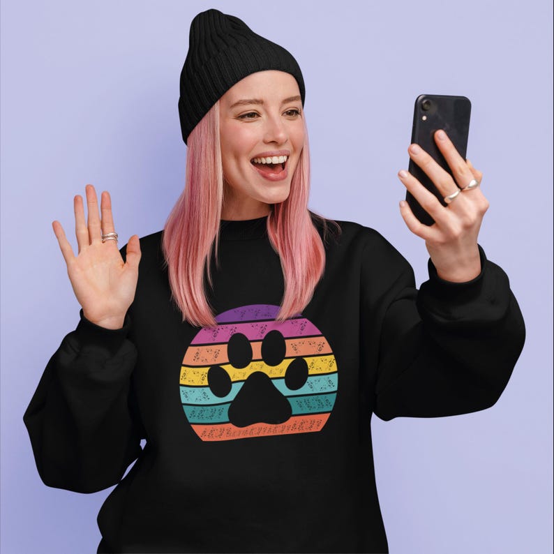 May include: A black sweatshirt with a colorful retro-style paw print graphic. The graphic features a rainbow-colored sunset with a paw print in the center. The text "Unconditional Love" is written around the paw print.