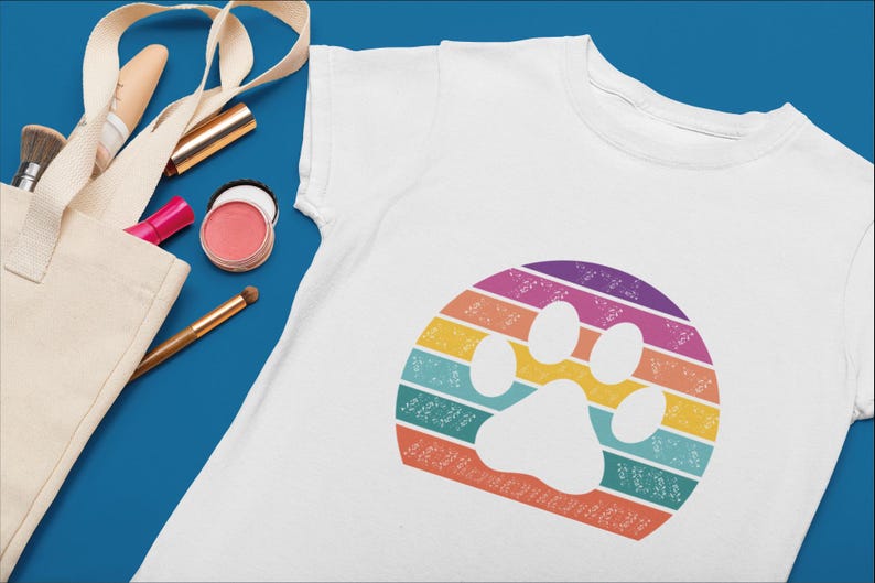 May include: White t-shirt with a rainbow paw print design. The paw print is in the center of the shirt and is surrounded by a rainbow of colors.