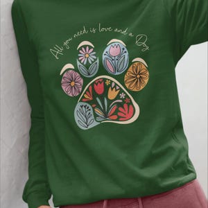 May include: Green long-sleeve t-shirt with a paw print design featuring colorful flowers and the text "All you need is love and a Dog".
