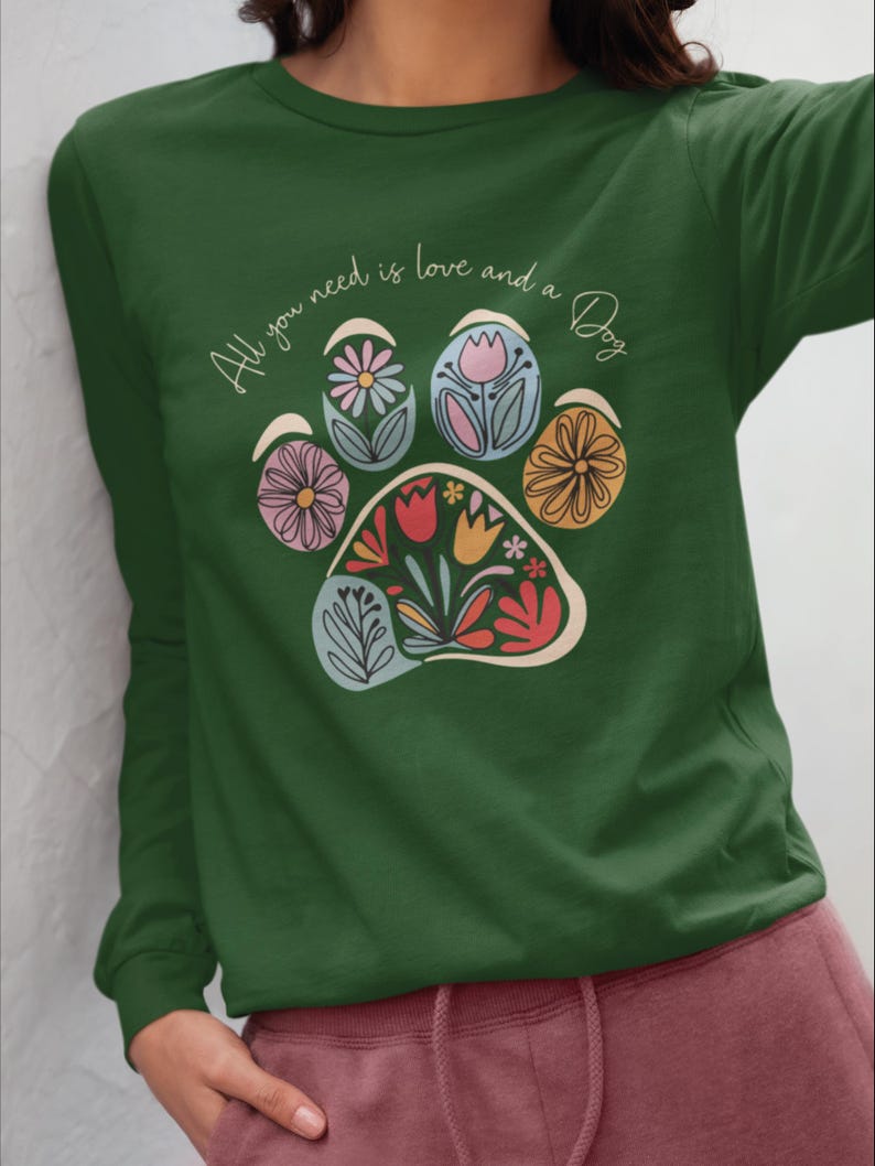 May include: Green long-sleeve t-shirt with a paw print design featuring colorful flowers and the text "All you need is love and a Dog".