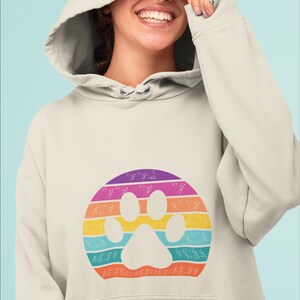 May include: A light beige hoodie with a rainbow paw print design. The paw print is surrounded by a circle of white flowers.