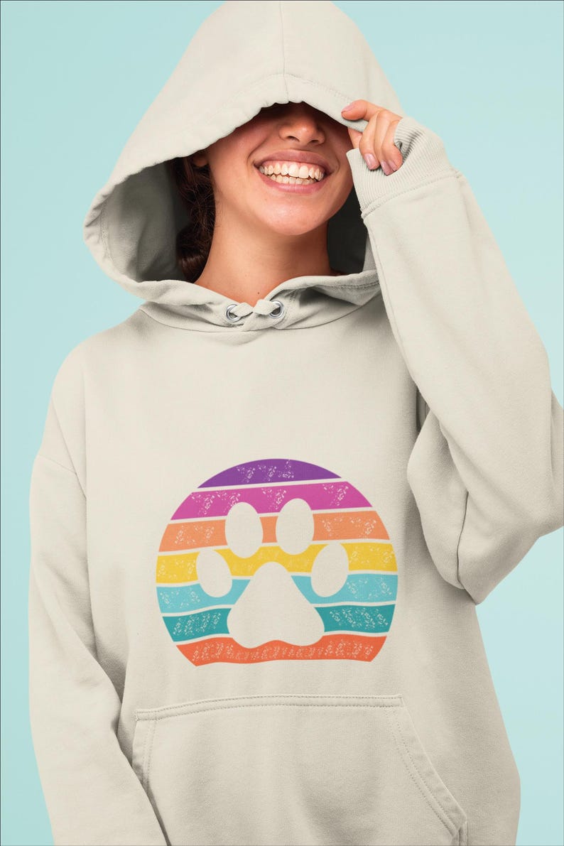 May include: A light beige hoodie with a rainbow paw print design. The paw print is surrounded by a circle of white flowers.