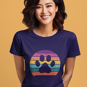 May include: A purple t-shirt with a rainbow paw print design. The paw print is surrounded by a circle of colorful stripes.