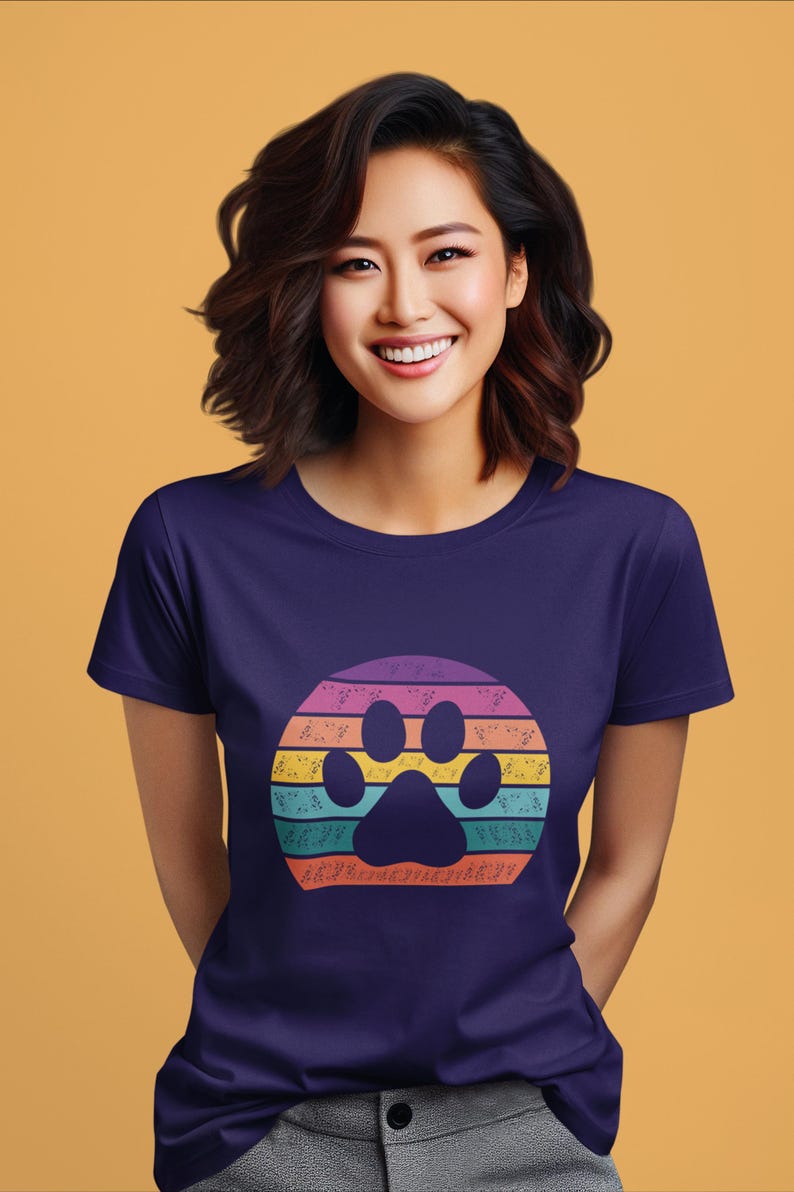 May include: A purple t-shirt with a rainbow paw print design. The paw print is surrounded by a circle of colorful stripes.