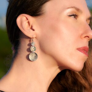 Puede incluir: Una mujer con pendientes de plata colgantes con tres discos redondos. Los pendientes son texturizados y tienen un acabado martillado.