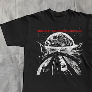May include: Black t-shirt with a white and red graphic design. The design features a cityscape inside a dome, a road, and the text "Tiberian Park, Transcending the Sky".