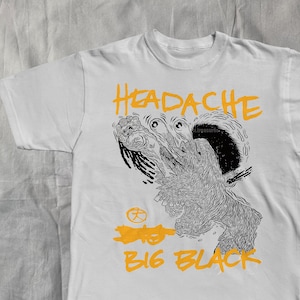 May include: White t-shirt with a graphic design in black and orange. The design features a stylized creature and the words "HEADACHE BIG BLACK". The shirt is made of a soft material.