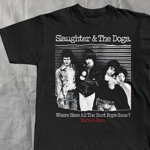 Könnte beinhalten: Schwarzes T-Shirt mit einem Schwarz-Weiß-Bild einer Band und dem Text "Slaughter & The Dogs." Unter dem Bild stehen die Worte "Where Have All The Boot Boys Gone?" und "You're A Bore" in Weiß.