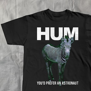 May include: Black t-shirt featuring a zebra illustration with the word "HUM" in white block letters above the zebra. Below the zebra, the text reads "YOU'D PREFER AN ASTRONAUT".