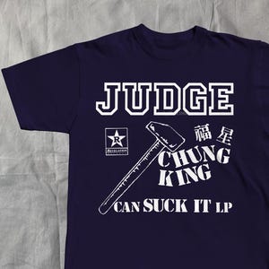 May include: A navy blue t-shirt with white text and graphics. The word "JUDGE" is at the top, with a hammer graphic and the words "CHUNG KING" and "CAN SUCK IT LP" below. A star logo is on the left.