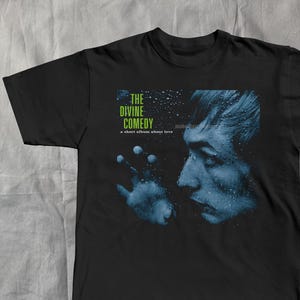 May include: Black t-shirt with a blue and white graphic. The graphic shows a side profile of a face and hand, with the text "THE DIVINE COMEDY" and "a short album about love".