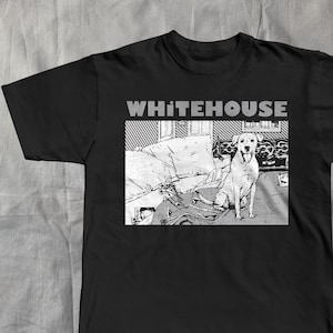 Op de afbeelding: Zwart t-shirt met een afbeelding van een hond op een bank en het woord "WHITEHOUSE" in grijs erboven. De hond is wit, de bank grijs en wit. Het ontwerp heeft een monochrome stripboekstijl.