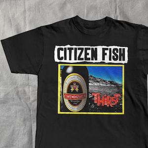 May include: Black t-shirt with a graphic featuring the text "CITIZEN FISH" above a rectangular image. The image includes a beer bottle and the word "Thirst" in red, set against a mountain landscape.