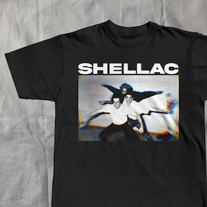 May include: Black t-shirt with the band name "SHELLAC" in white block letters above a black and white image of three people. The image has a slight color distortion effect.