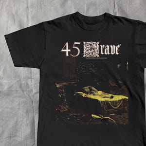 May include: Black t-shirt featuring the band name "45 Grave" in white, with an ornate emblem. The shirt's graphic depicts a person lying on a bed, with a yellow blanket, in a dimly lit room. The album title "Sleepwalk Treasures" is also visible.