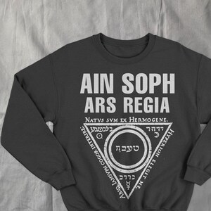 May include: Dark grey sweatshirt featuring white text and a triangular graphic. The text includes "AIN SOPH ARS REGIA" and other phrases in a stylized font. The graphic features a circle and other symbols.
