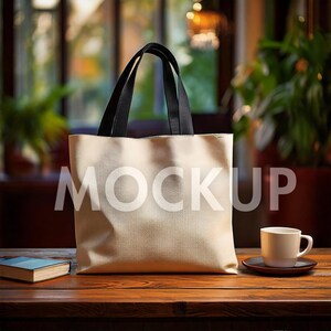 May include: A white canvas tote bag with black handles. The bag is sitting on a wooden table with a white coffee cup and saucer.