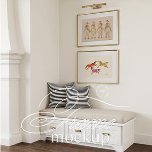 May include: A white storage bench with a beige cushion and two black and white striped pillows. Above the bench are two gold-framed prints: one showing four figures on horseback in brown tones, and another with three colorful horses in motion.
