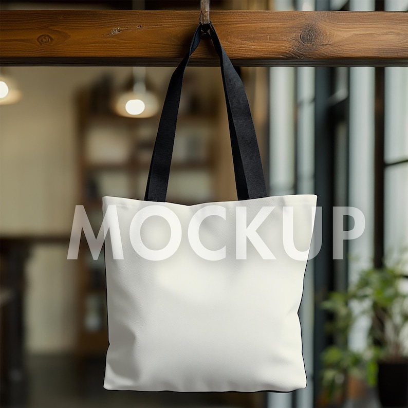 May include: A white tote bag with black handles hangs from a wooden beam. The word "MOCKUP" is printed across the front of the bag in a transparent font. The background is blurred, suggesting an indoor setting.