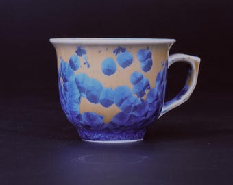 Puede incluir: Una taza de té de cerámica con un patrón floral azul y amarillo. La taza tiene una forma redondeada y un asa.
