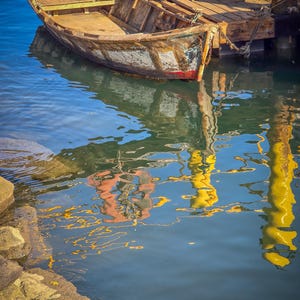 An old rowboat is docked at a pier, its reflection visible in the shimmering water below, along with the scenes above.