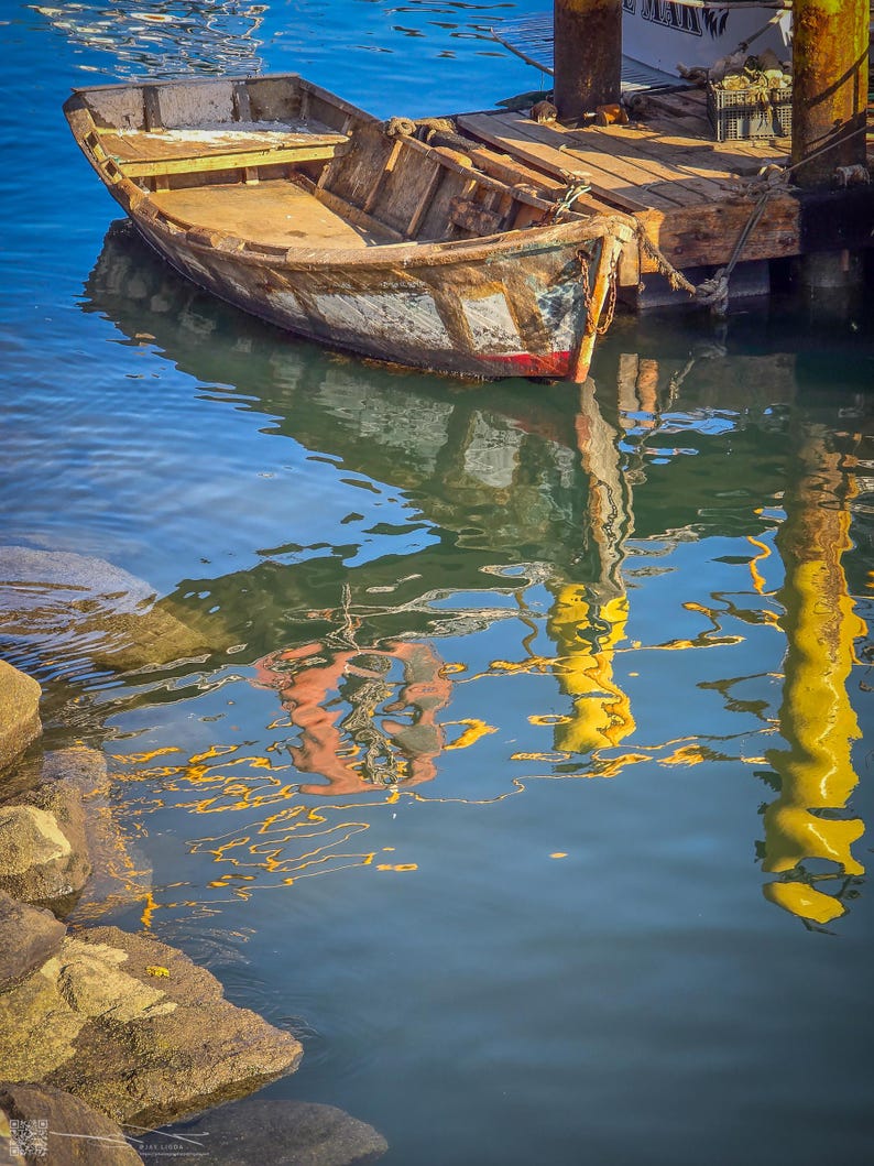 An old rowboat is docked at a pier, its reflection visible in the shimmering water below, along with the scenes above.
