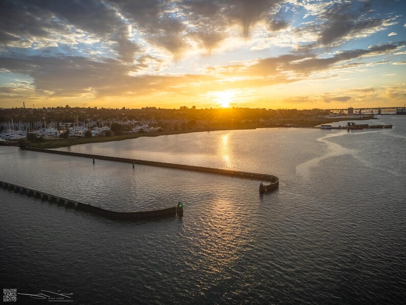 The warm yellow sun rises above the horizon, its light reflecting on the water near the entrance to the Benicia Marina.