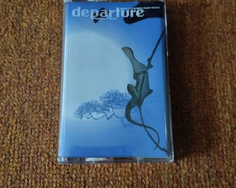 May include: A cassette tape with the word "departure" in white text. The cover art features a blue background with a black and gray illustration of a figure holding a flag, and a tree. The cassette is in a clear plastic case.