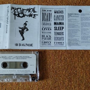 May include: A white cassette tape with a black label. The label features the band name "My Chemical Romance" and the album title "The Black Parade". The cassette tape has a clear plastic case and a silver metal backing.