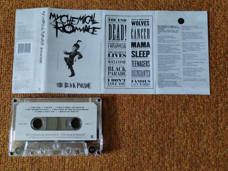 May include: A white cassette tape with a black label. The label features the band name "My Chemical Romance" and the album title "The Black Parade". The cassette tape has a clear plastic case and a silver metal backing.