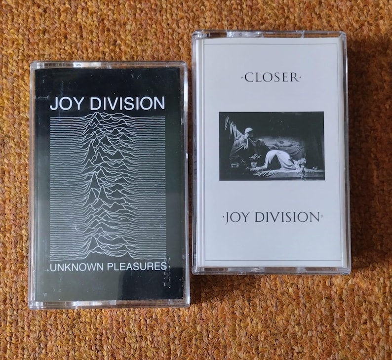 Puede incluir: Dos cintas de casete de Joy Division. La primera cinta es "Unknown Pleasures" y presenta un gr&aacute;fico en blanco y negro de una forma de onda. La segunda cinta es "Closer" y presenta una foto en blanco y negro de una persona arrodillada en el suelo.