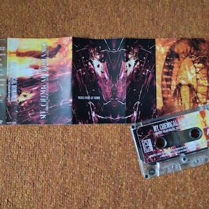 May include: A clear cassette tape and album art for the band My Chemical Romance. The album art is a mix of orange, red, and black. The cassette tape has the band's name and album title printed on it.