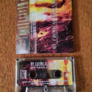 May include: A cassette tape and its case featuring the album art for "I Brought You My Bullets, You Brought Me Your Love" by My Chemical Romance. The case has a red and orange design with the band's name. The cassette tape is clear.