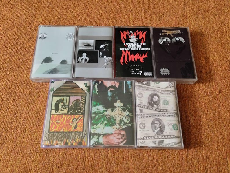 May include: Collection of seven cassette tapes with various cover designs. The covers feature images and text, including the phrase "I Want to Die in New Orleans." The tapes are in clear plastic cases.