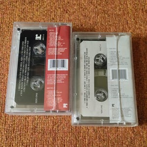May include: Two cassette tapes, one red and one white, featuring My Chemical Romance's albums "The Black Parade" and "Three Cheers for Sweet Revenge". The tapes are in clear plastic cases with the album titles and track lists printed on the back.
