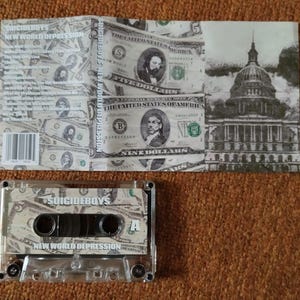 May include: A cassette tape and its cover featuring a design of US dollar bills. The cassette tape has the text "SUICIDEBOYS" and "NEW WORLD DEPRESSION". The cover also displays the text "SUICIDEBOYS" and a grayscale image of a building.