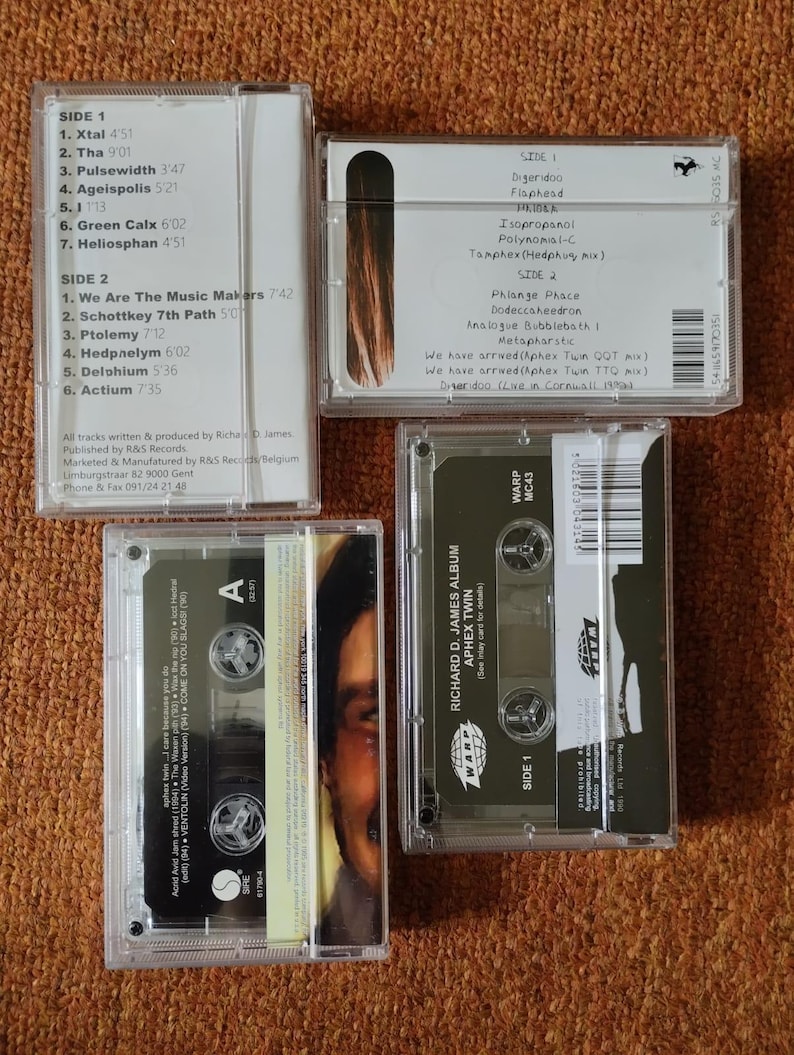 May include: Four clear cassette tapes with labels. The tapes are labeled with the names of the artists and albums. The tapes are on a brown surface.