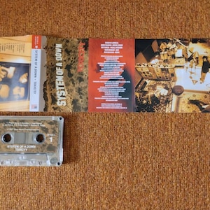 May include: A clear cassette tape case with a black and white label that reads "System of a Down Toxicity". The cassette tape is inside the case and is labeled with the band's name and album title.