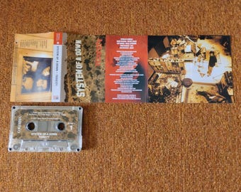 May include: A clear cassette tape case with a black and white label that reads "System of a Down Toxicity". The cassette tape is inside the case and is labeled with the band's name and album title.