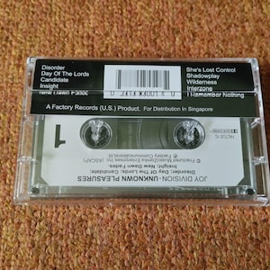 Puede incluir: Una cinta de casete negra en una caja de pl&aacute;stico transparente. La cinta est&aacute; etiquetada como "Joy Division - Unknown Pleasures" y enumera canciones que incluyen "Disorder", "Day of the Lords", "Candidate", "Insight", "She's Lost Control", "Shadowplay", "Wilderness", "Interzone" e "I Remember Nothing". La cinta es un producto de Factory Records (U.S.) para distribuci&oacute;n en Singapur.