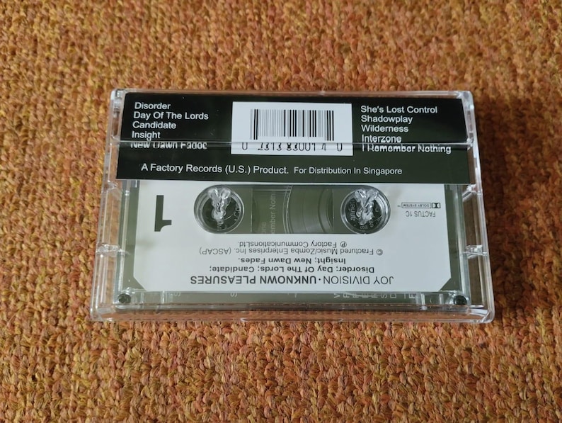 Puede incluir: Una cinta de casete negra en una caja de pl&aacute;stico transparente. La cinta est&aacute; etiquetada como "Joy Division - Unknown Pleasures" y enumera canciones que incluyen "Disorder", "Day of the Lords", "Candidate", "Insight", "She's Lost Control", "Shadowplay", "Wilderness", "Interzone" e "I Remember Nothing". La cinta es un producto de Factory Records (U.S.) para distribuci&oacute;n en Singapur.
