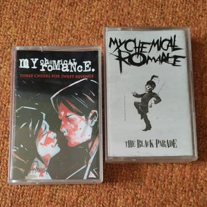 May include: Two cassette tapes, one black and one white. The black cassette tape has the text "My Chemical Romance" and "Three Cheers for Sweet Revenge" on it. The white cassette tape has the text "My Chemical Romance" and "The Black Parade" on it.