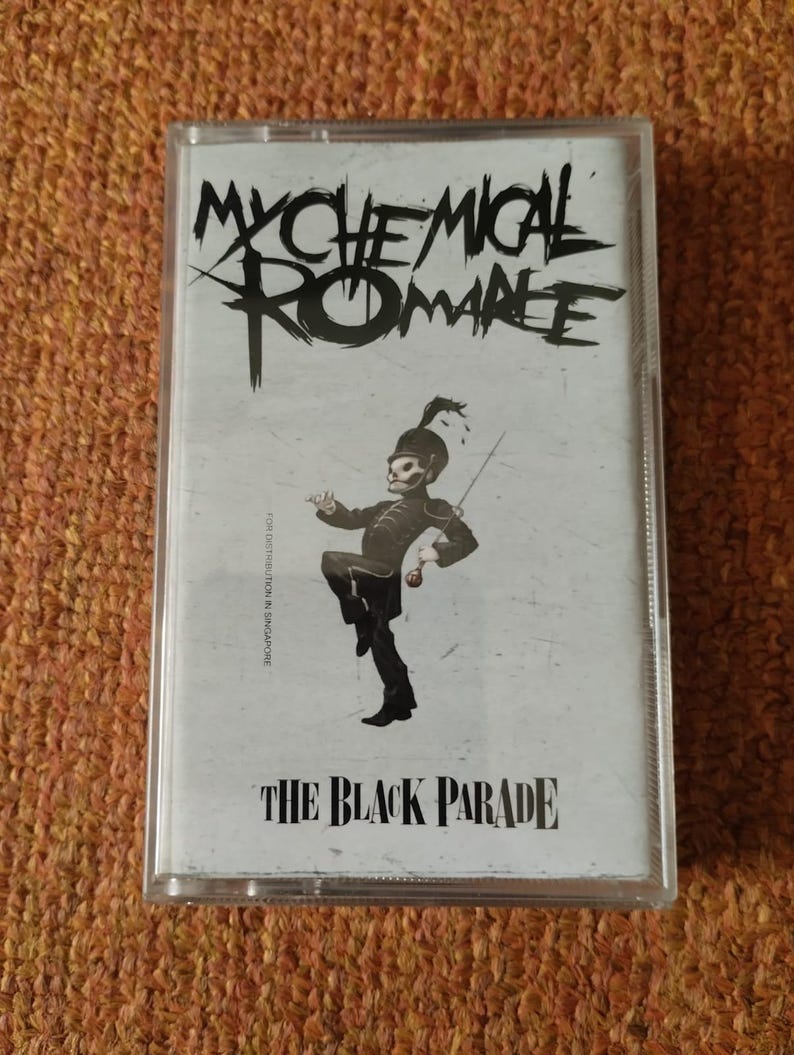 May include: A cassette tape case featuring a black and white illustration of a cartoon skeleton in military attire. The text "My Chemical Romance" is printed in black at the top of the case. The text "The Black Parade" is printed in black at the bottom of the case.