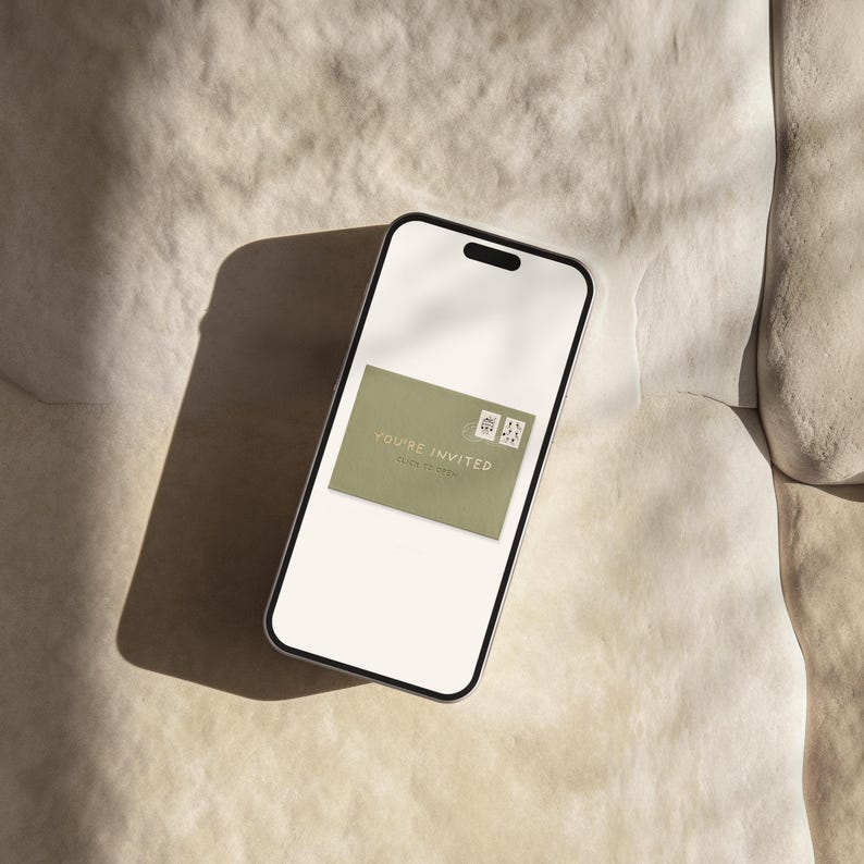May include: A smartphone displays a digital invitation. The invitation is a sage green rectangle with the words "YOU'RE INVITED" and two small postage stamp graphics. The phone is on a textured, off-white surface.