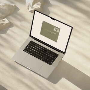 May include: A silver laptop displays a digital invitation on its screen. The invitation is a muted green color with the words "YOU'RE INVITED" and two small postage stamps. The laptop is on a light-colored surface.