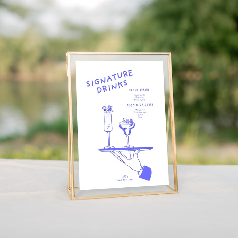 K&ouml;nnte beinhalten: Ein goldfarbener Rahmen mit einem wei&szlig;en Hintergrund und blauem Text. Das Schild lautet "Signature Drinks" und listet zwei Getr&auml;nke auf: "Peach Bellini" und "Frozen Daiquiris". Das Schild zeigt auch eine Hand, die ein Tablett mit zwei Gl&auml;sern Getr&auml;nke h&auml;lt.