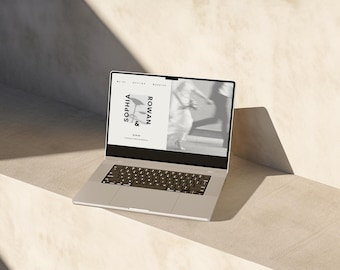 May include: A silver laptop displays a wedding invitation with the names "SOPHIA & ROWAN" in a minimalist design. The screen shows a blurred image of a couple. The laptop is on a light-colored surface.