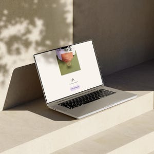 May include: A silver laptop displaying a wedding invitation design. The screen shows an open envelope with invitation cards. The laptop is on a light-colored surface, with shadows from overhead.