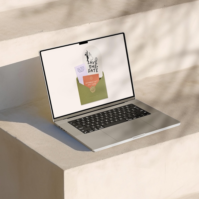 May include: A silver laptop displays a wedding invitation design. The design includes a "Save the Date" graphic, a green envelope, and two cards. The cards have text and a circular design. The laptop is on a white surface.